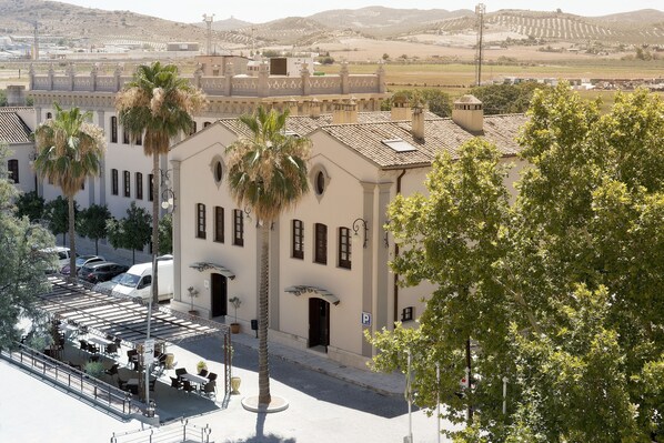 A building with a courtyard, palm trees, and a parking area. - Hotel El Carmen (Puente Genil)