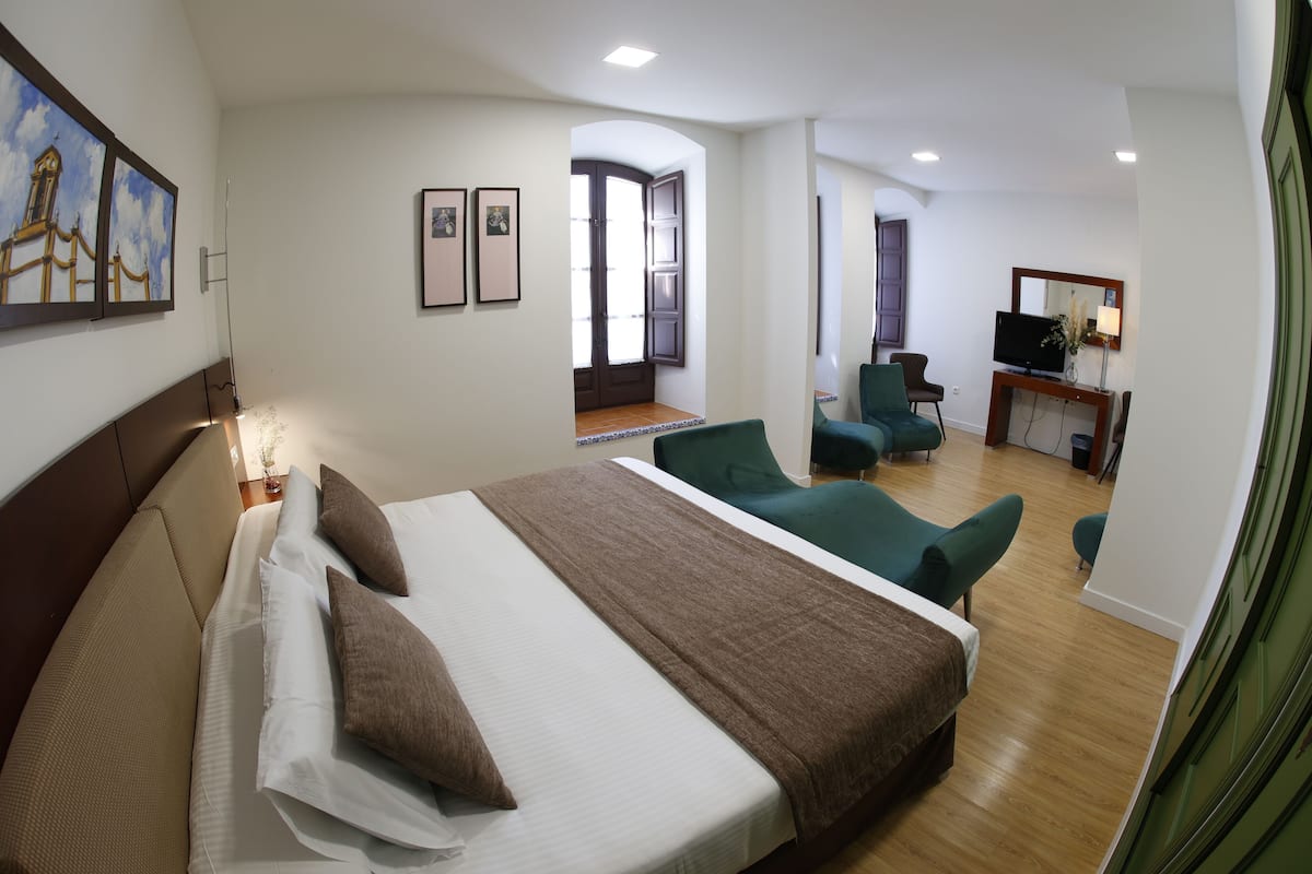 A hotel room with a large bed, a desk with a TV, and a seating area with chairs.