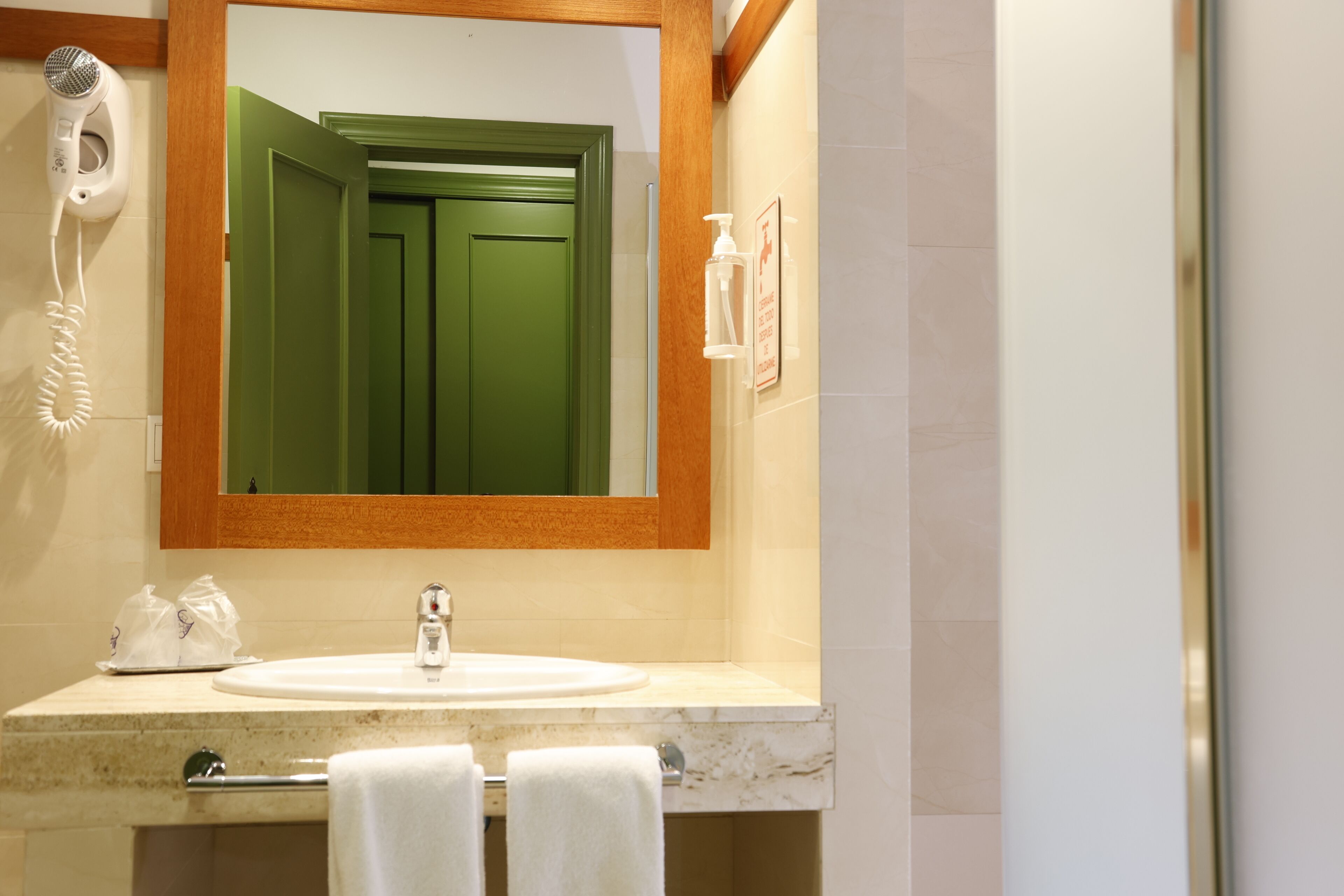 Un baño con un espejo grande, un lavabo, un secador de pelo y un perchero para toallas.