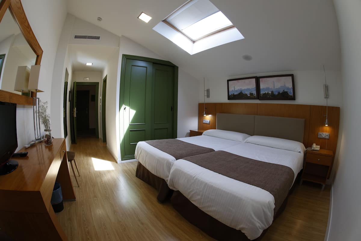 A bedroom with a large bed, a desk with a computer, a green wardrobe, and a skylight.