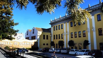 Un hotel con fachada amarilla, coches aparcados y un cielo azul despejado.