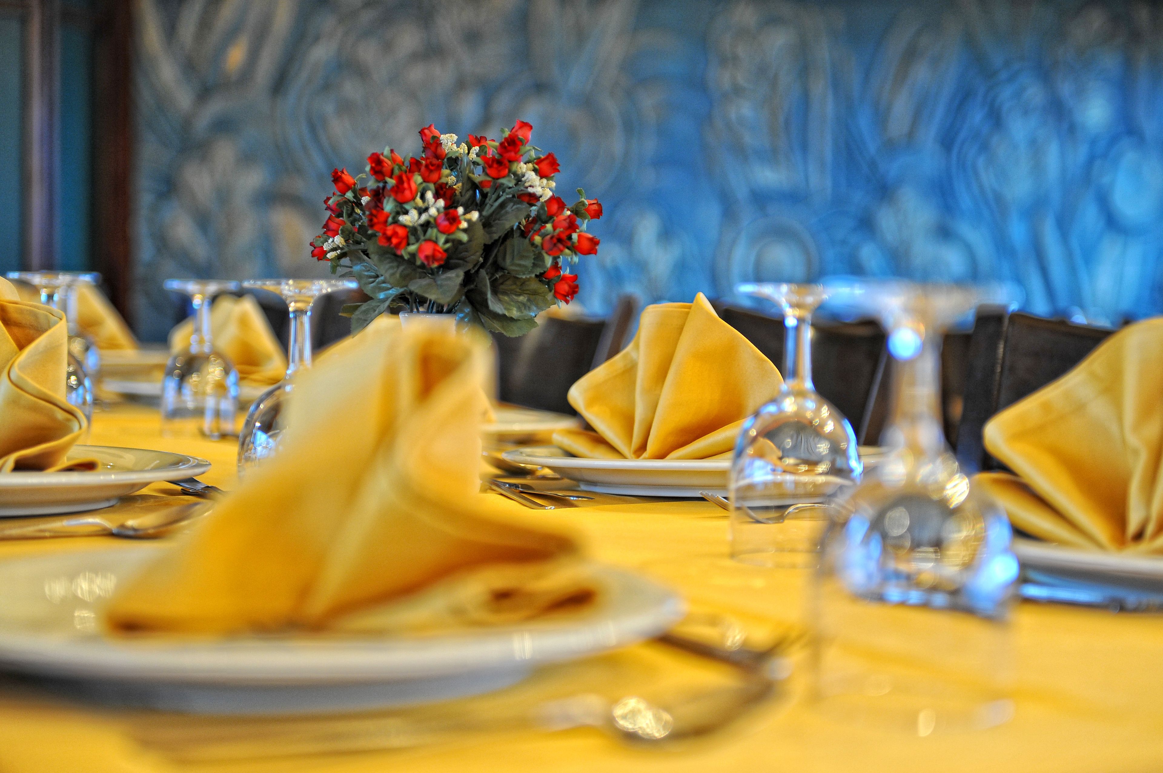 A dining table set with yellow napkins, clear glassware, and a centerpiece of red roses.