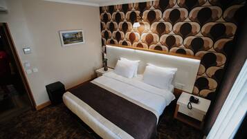 A neatly arranged hotel room with a large bed, a bedside table, a nightstand, and a patterned wall.