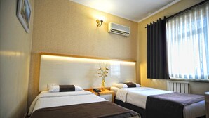 A hotel room with two beds, a bedside table with a lamp, an air conditioner, and a window with curtains. - Horon Hotel (Trabzon)