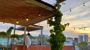 Een terras op het dak met een houten pergola, lichtjes en een uitzicht over de stad.