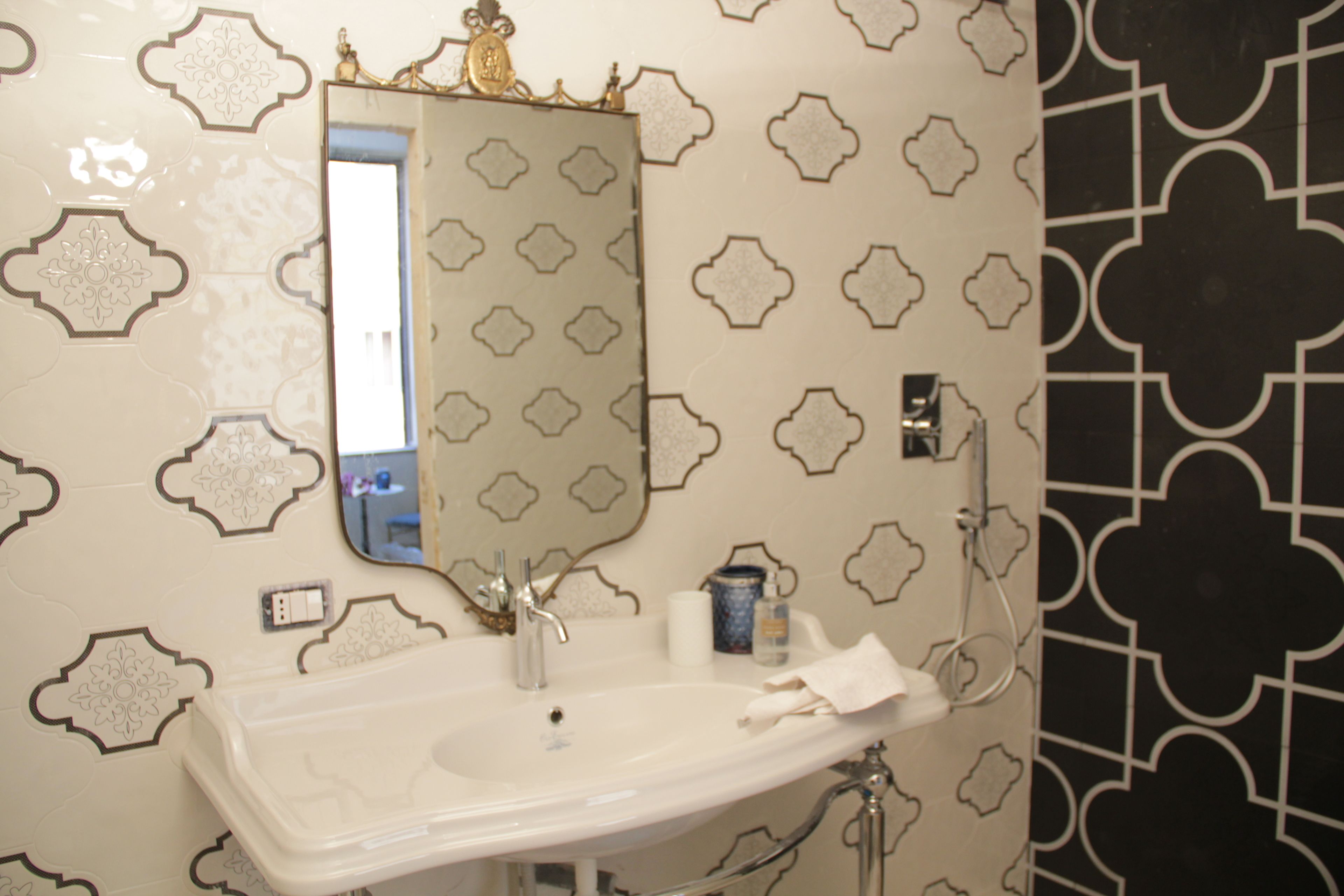 A bathroom with a white sink, a mirror, and a patterned wall.