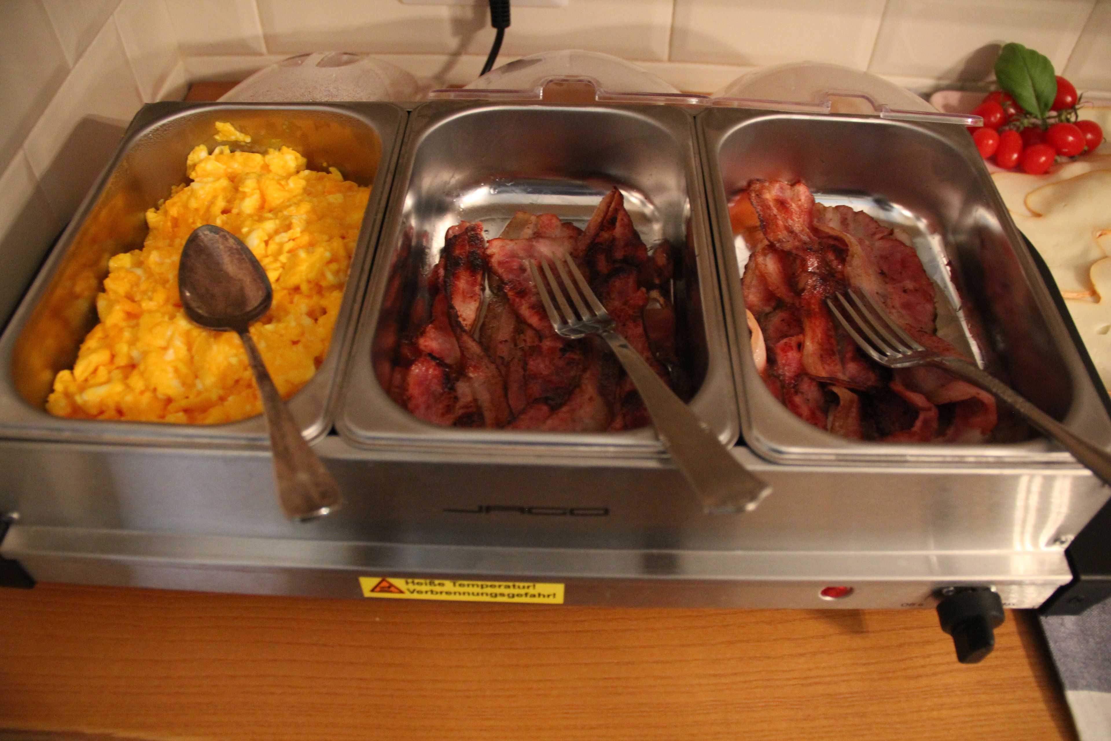 A buffet with scrambled eggs, bacon, and a warning label on the equipment.