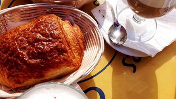 Un tavolo con un cornetto, un pasticcino e un bicchiere di una bevanda cremosa, probabilmente caffè o cioccolata calda.