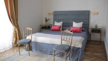 Un dormitorio ordenado con una cama grande, dos mesitas de noche, una silla y una pequeña mesa con un florero.