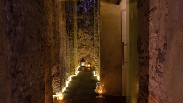 A narrow, dimly lit corridor with stone walls and a pathway lined with candles. - Ingrami Suites (Rome)