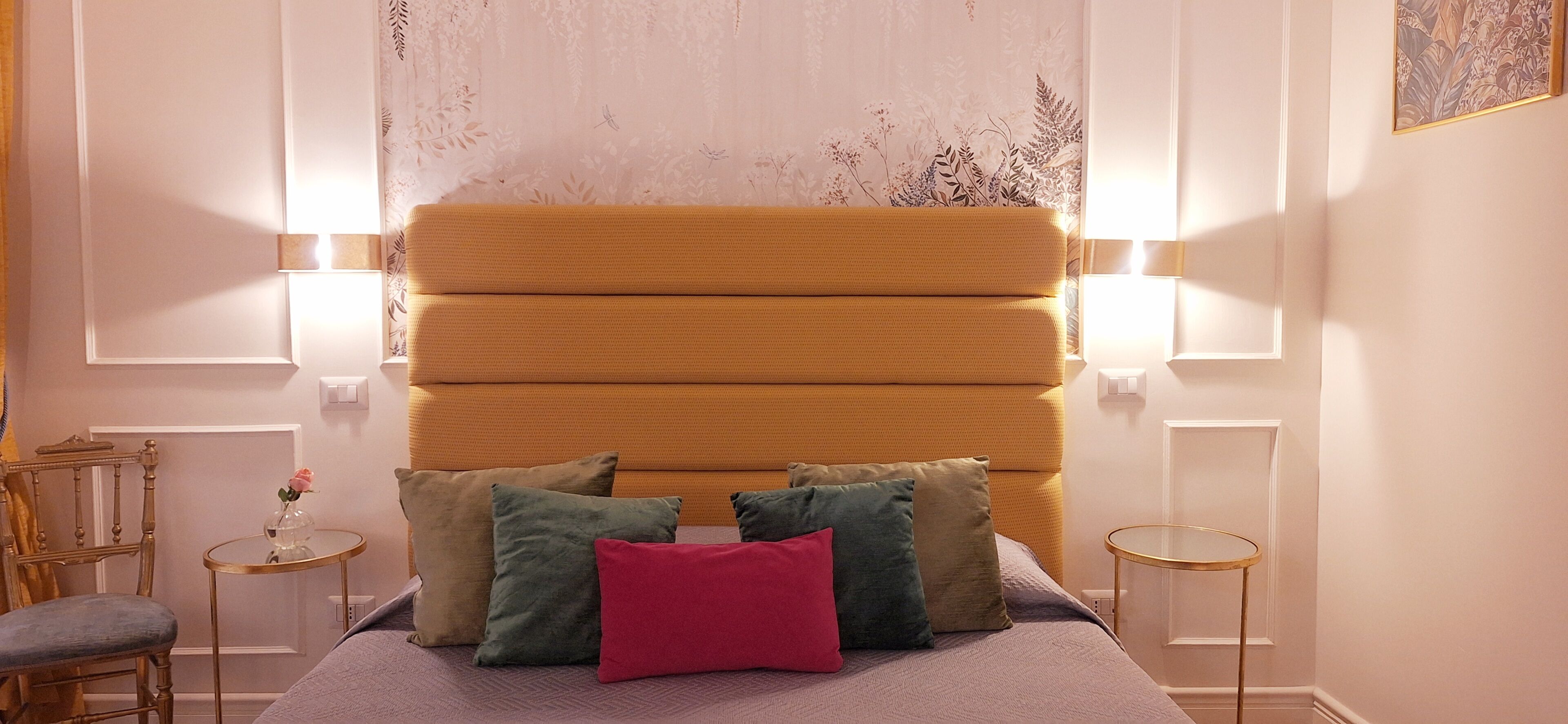 A bedroom with a large bed, multiple pillows, two bedside tables, a chair, and a small table with a vase.