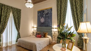 A bedroom with a large bed, a chandelier, a painting, and curtains. - Ingrami Suites (Rome)