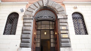 A building entrance with a stone archway, a wooden door, and two windows with metal grilles. - Ingrami Suites (Rome)