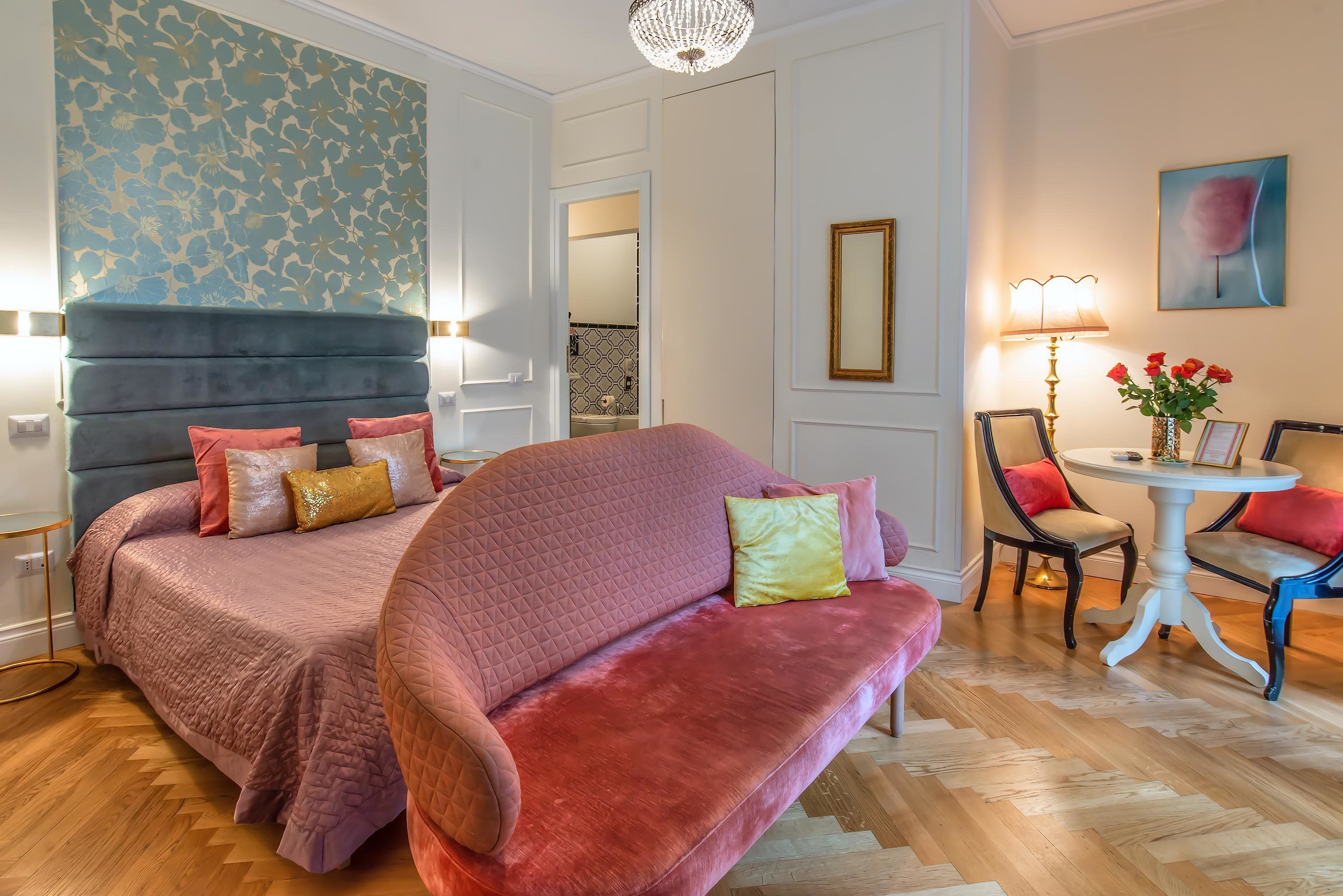 A bedroom with a large bed, a chaise lounge, a small table with a lamp, and a chair.