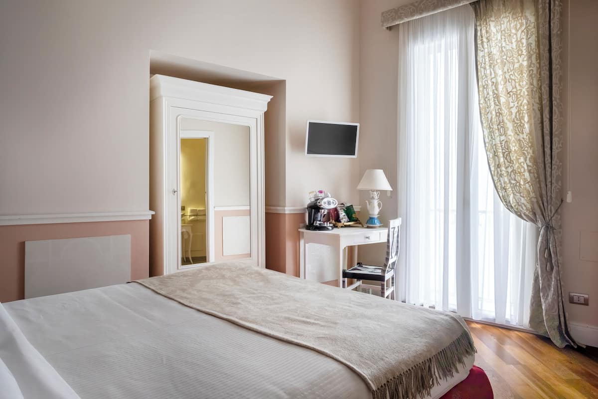 Une chambre d’hôtel avec un lit, un bureau, une chaise, une télévision et une fenêtre avec des rideaux.
