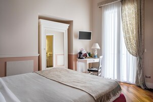 Une chambre d’hôtel avec un lit, un bureau, une chaise, une télévision et une fenêtre avec des rideaux.