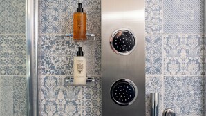 A bathroom with patterned tiles, a shower with a handheld showerhead, and two bottles of shampoo and conditioner on a shelf. - Dimora Bellini residenza d' epoca (Palermo)