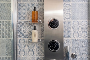 A bathroom with patterned tiles, a shower with a handheld showerhead, and two bottles of shampoo and conditioner on a shelf.