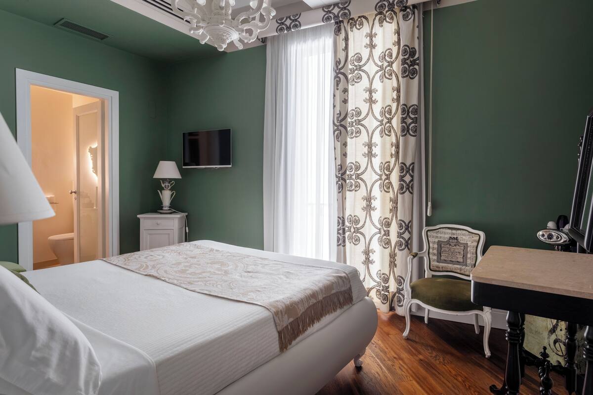 Une chambre à coucher comprenant un lit, un bureau, une chaise, un téléviseur et une porte donnant sur une salle de bain.