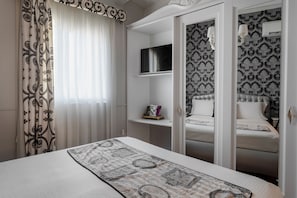 A bedroom with a bed, a wardrobe, a mirror, and a window with curtains.