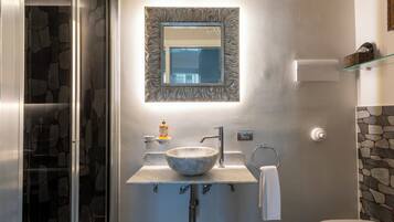Un baño con pared de piedra, lavamanos de mármol, espejo y repisa de vidrio.