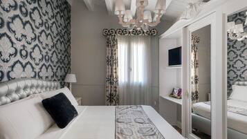 A hotel room with a large bed, a chandelier, a TV, and patterned wallpaper.