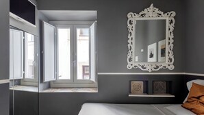 A bedroom with a bed, a large mirror, a window, and a shelf with decorative items. - Dimora Bellini residenza d' epoca (Palermo)