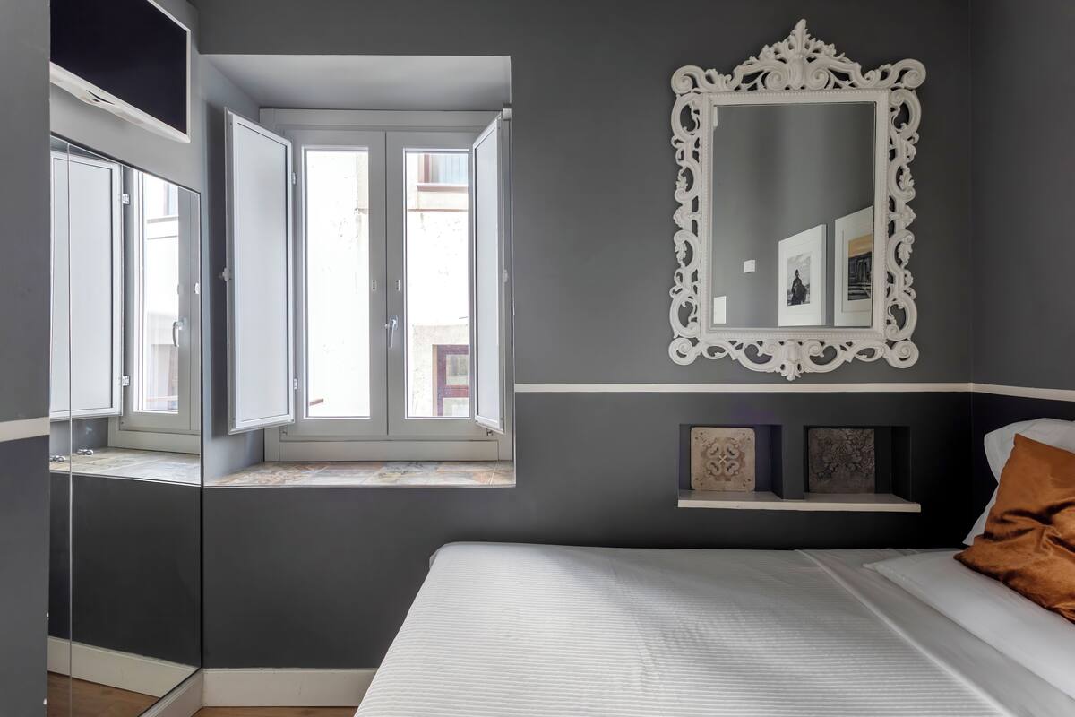 Une chambre à coucher comprenant un lit, un grand miroir, une fenêtre et une étagère avec des objets décoratifs.