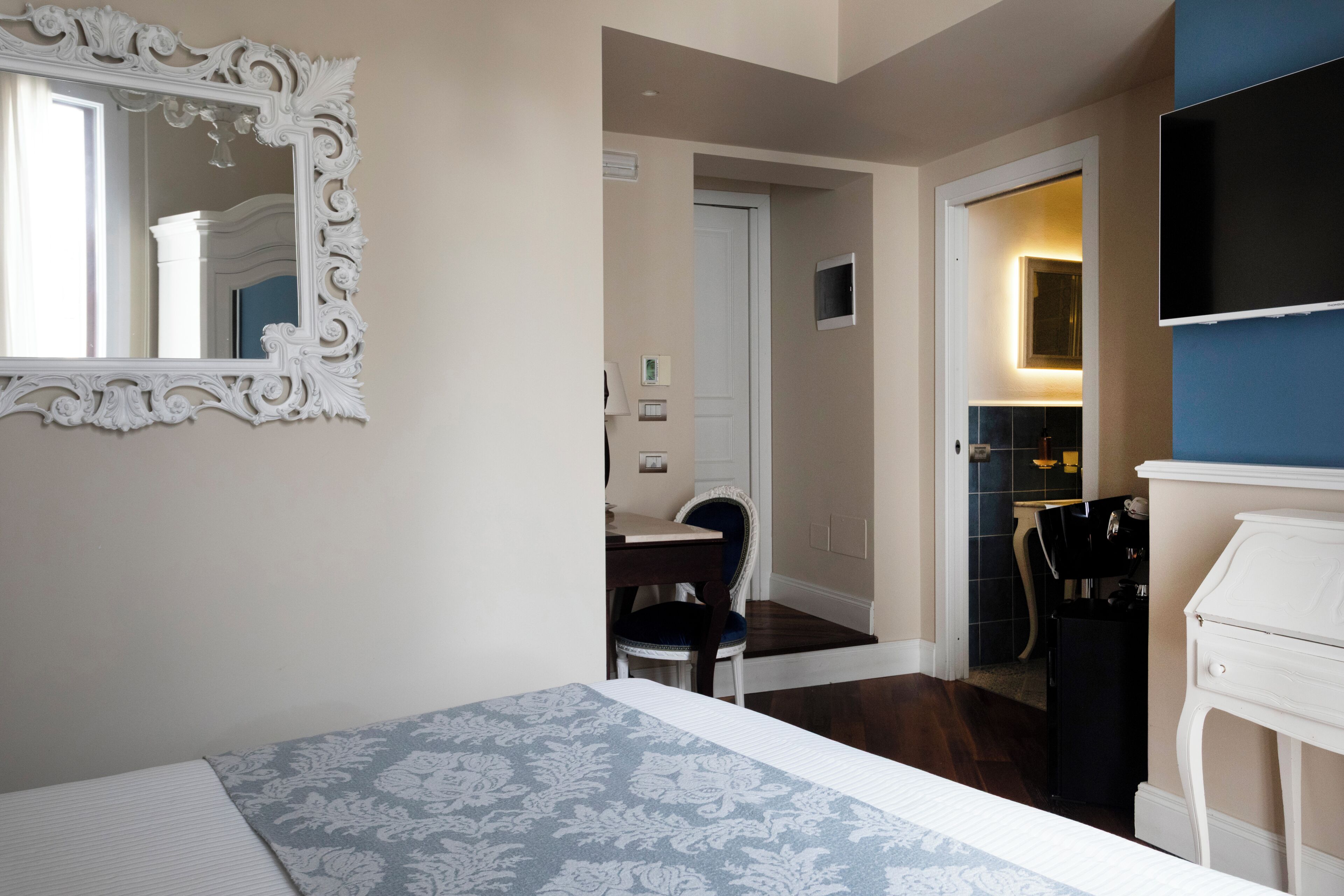 Une chambre d’hôtel avec un lit, un miroir, une télévision, un bureau et une chaise.