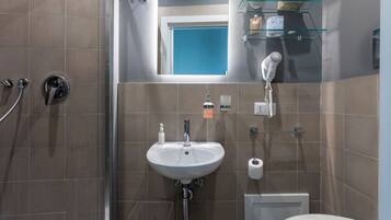 A bathroom with a sink, a mirror, a shower, and a toilet.