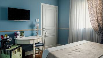 A bedroom with a bed, a desk with a chair, a television on the wall, a door, and a window with curtains.