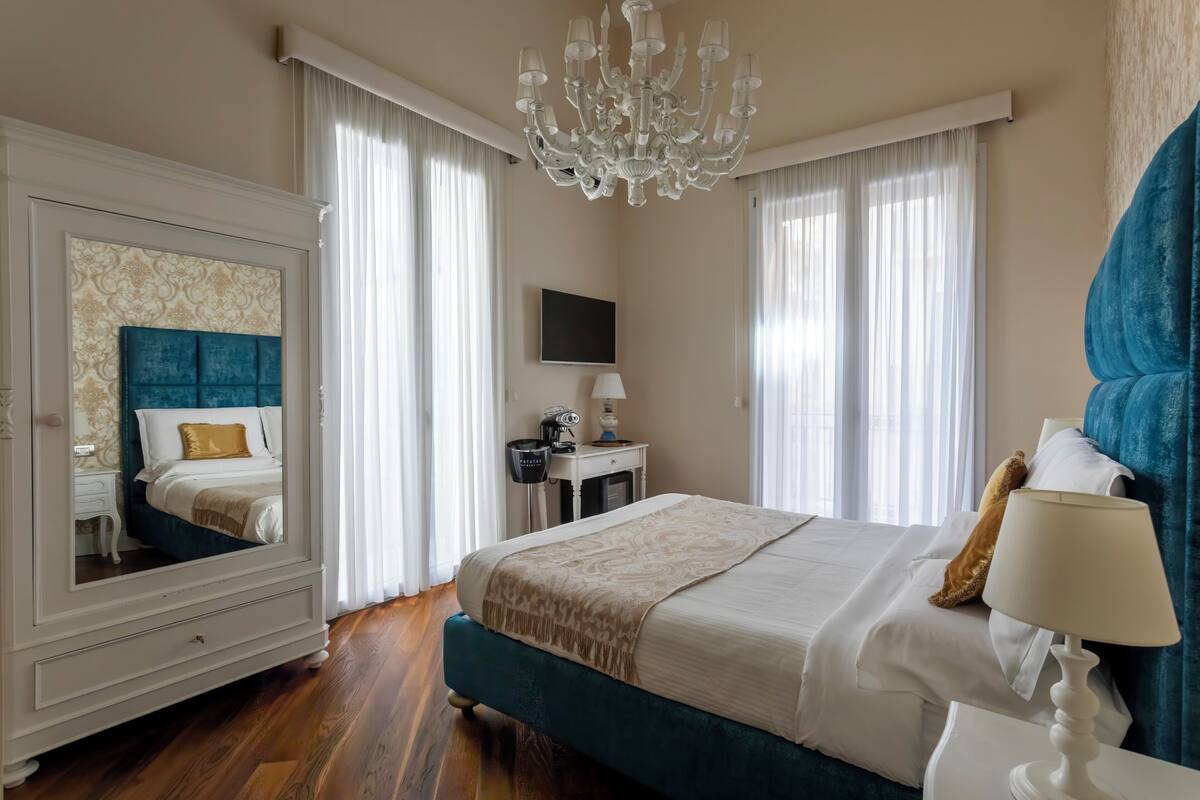 Une chambre d’hôtel avec un grand lit, un miroir, un lustre, une télévision et un bureau avec une lampe.