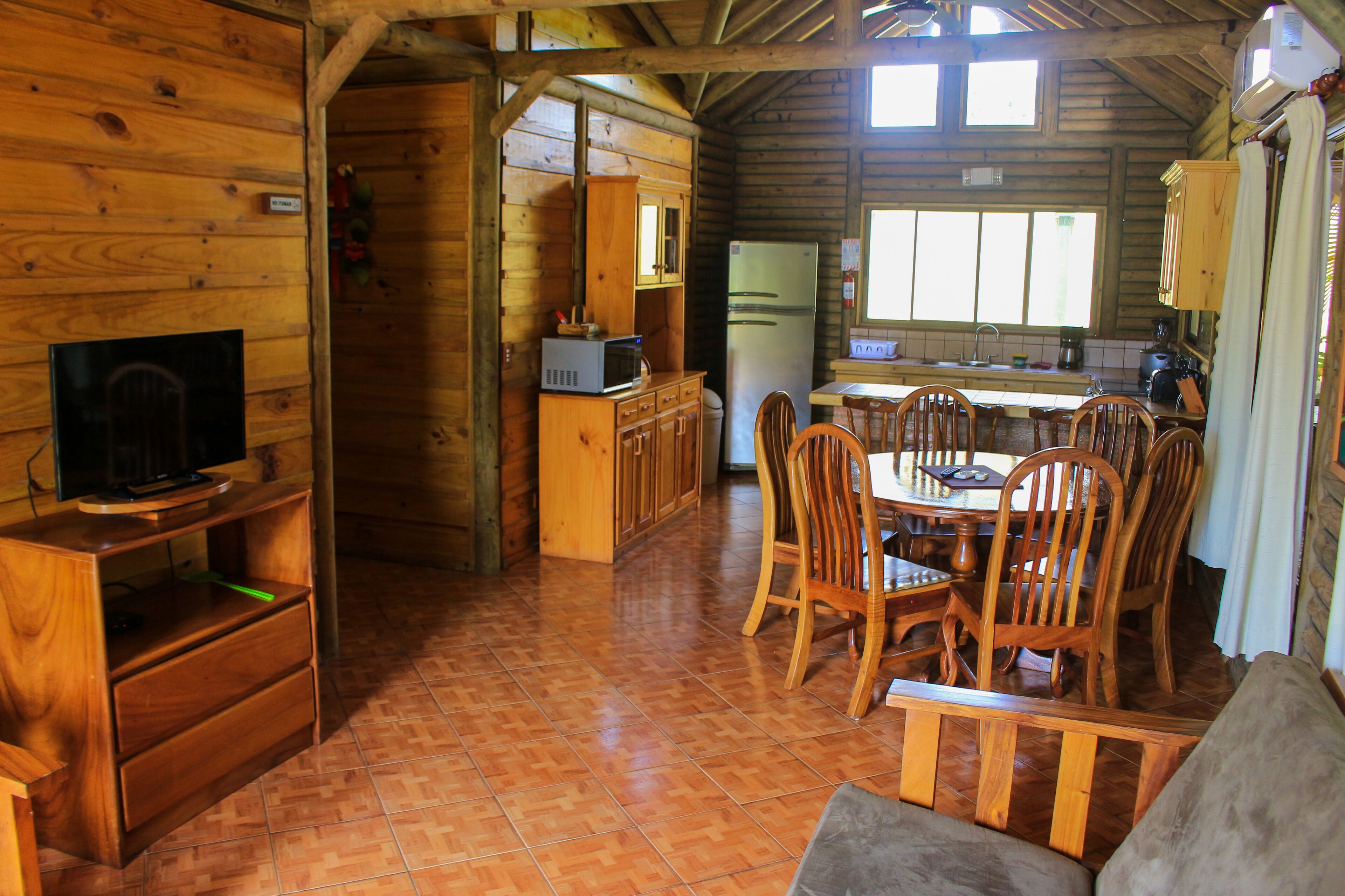 L’intérieur d’un chalet en bois comprend un coin repas, une cuisine et un téléviseur posé sur un meuble en bois.