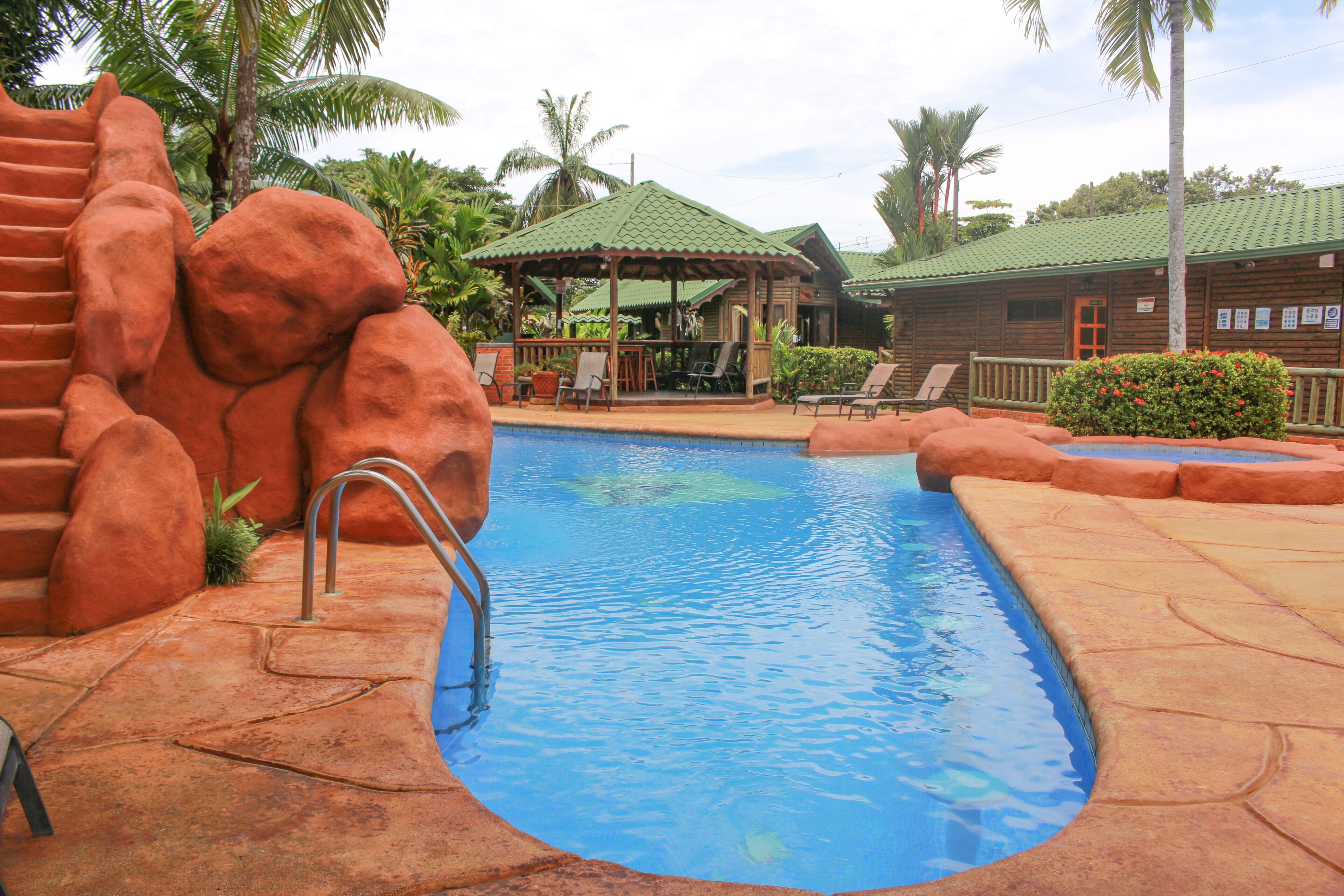 A pool area with a clear blue pool, a wooden deck, and a gazebo.