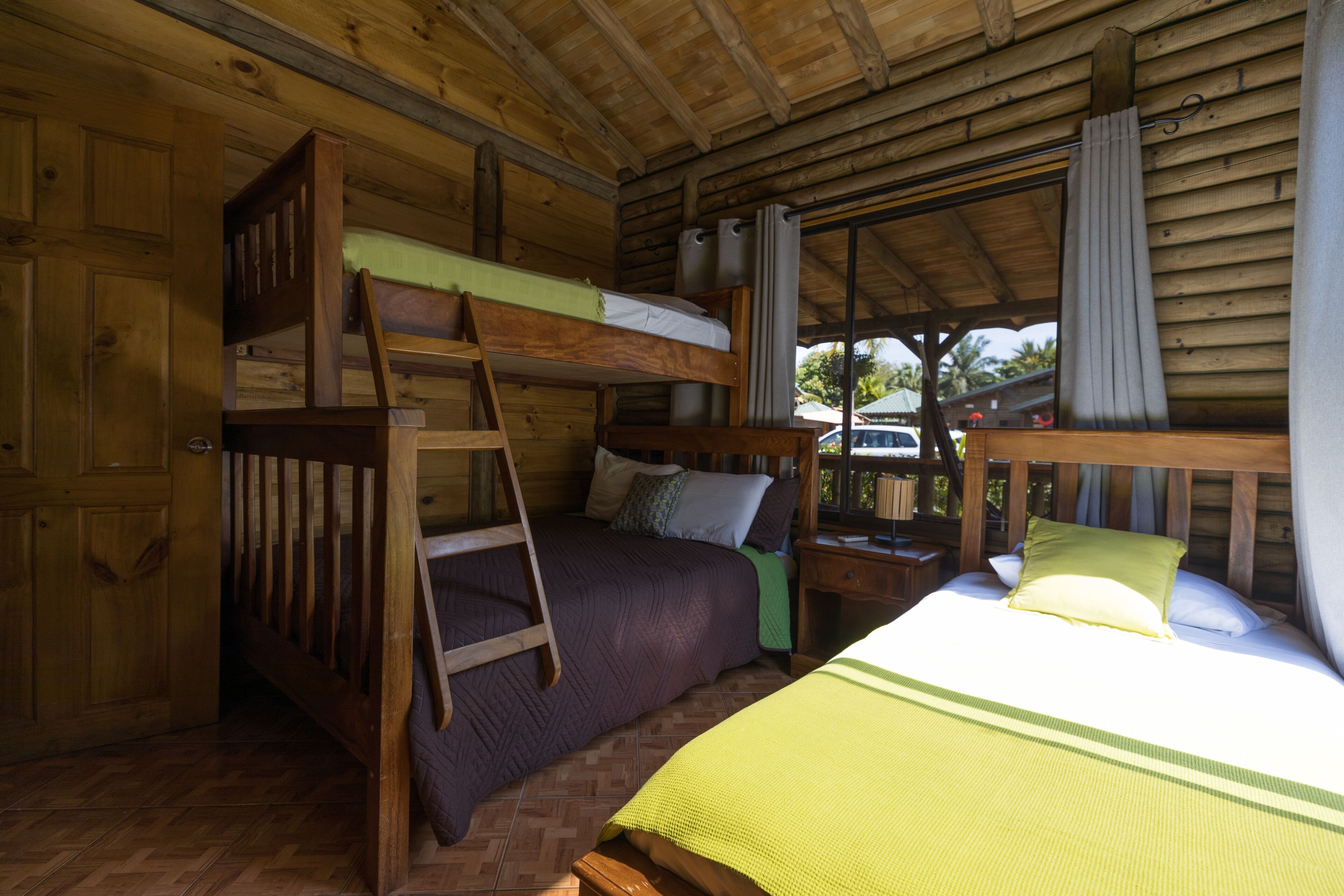 Een kamer in chaletstijl met een stapelbed, een ladder, een houten bureau en een raam met gordijnen.