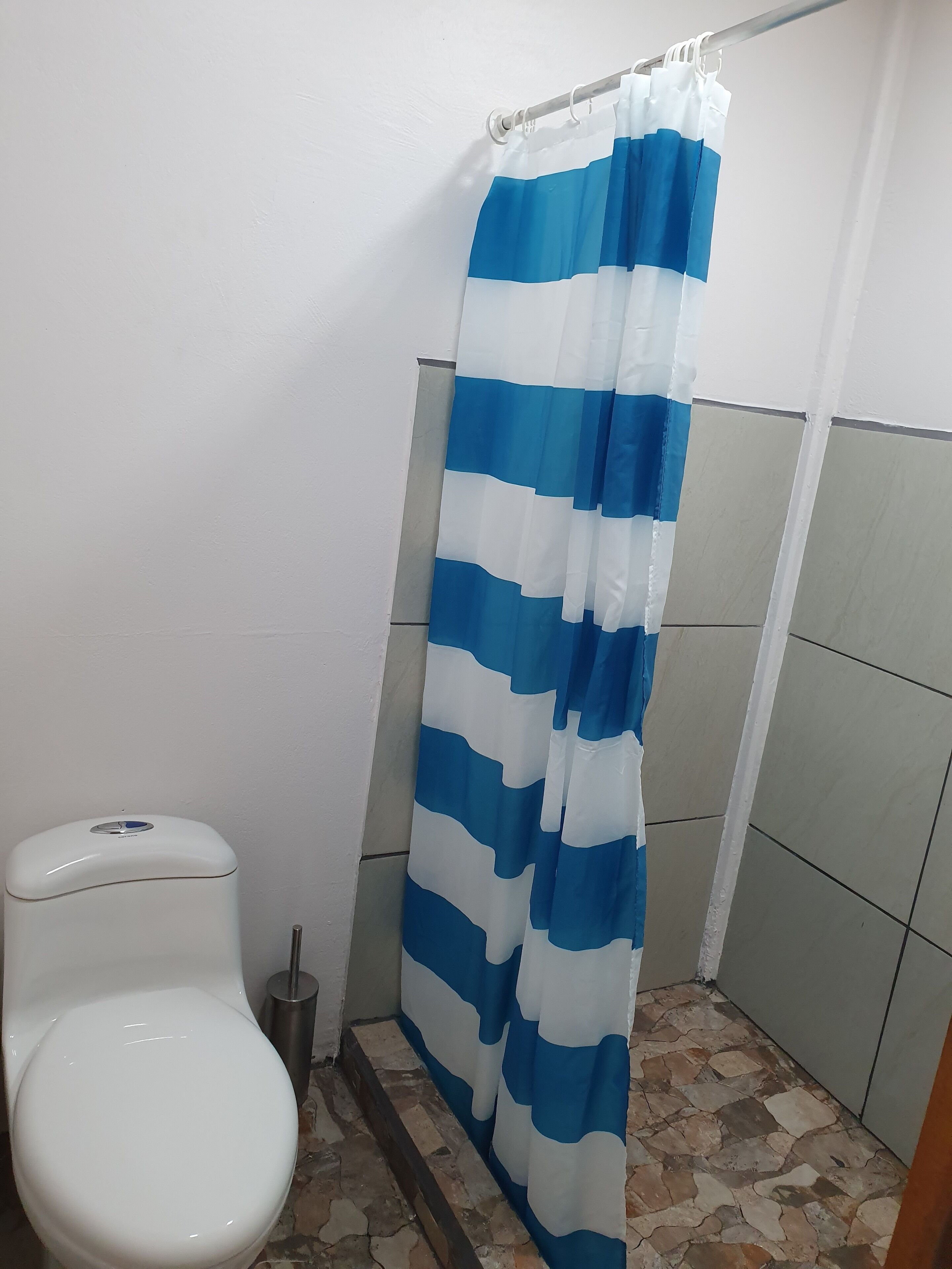 A bathroom with a white toilet, a blue and white striped shower curtain, and tiled walls.