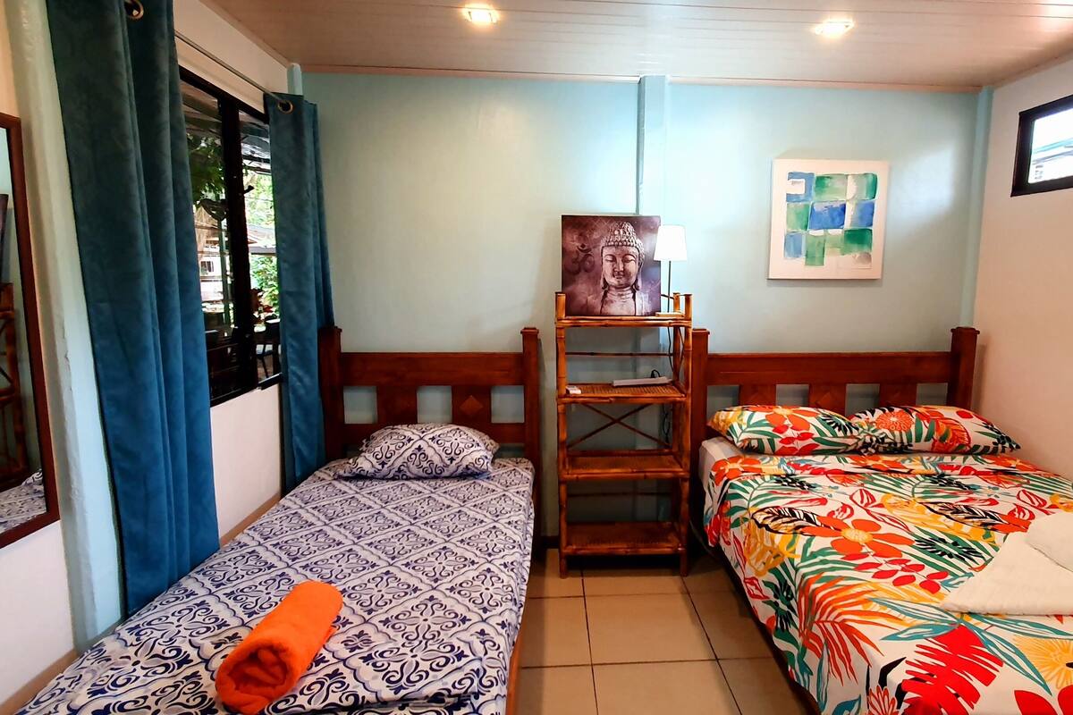 A room with two beds, a wooden headboard, a small table, and a Buddha painting on the wall.