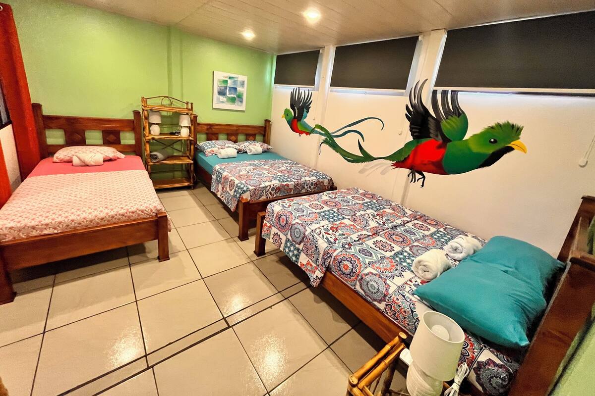 A hotel room with two single beds, a wooden headboard, a shelf with decorative items, and a mural of a bird on the wall.