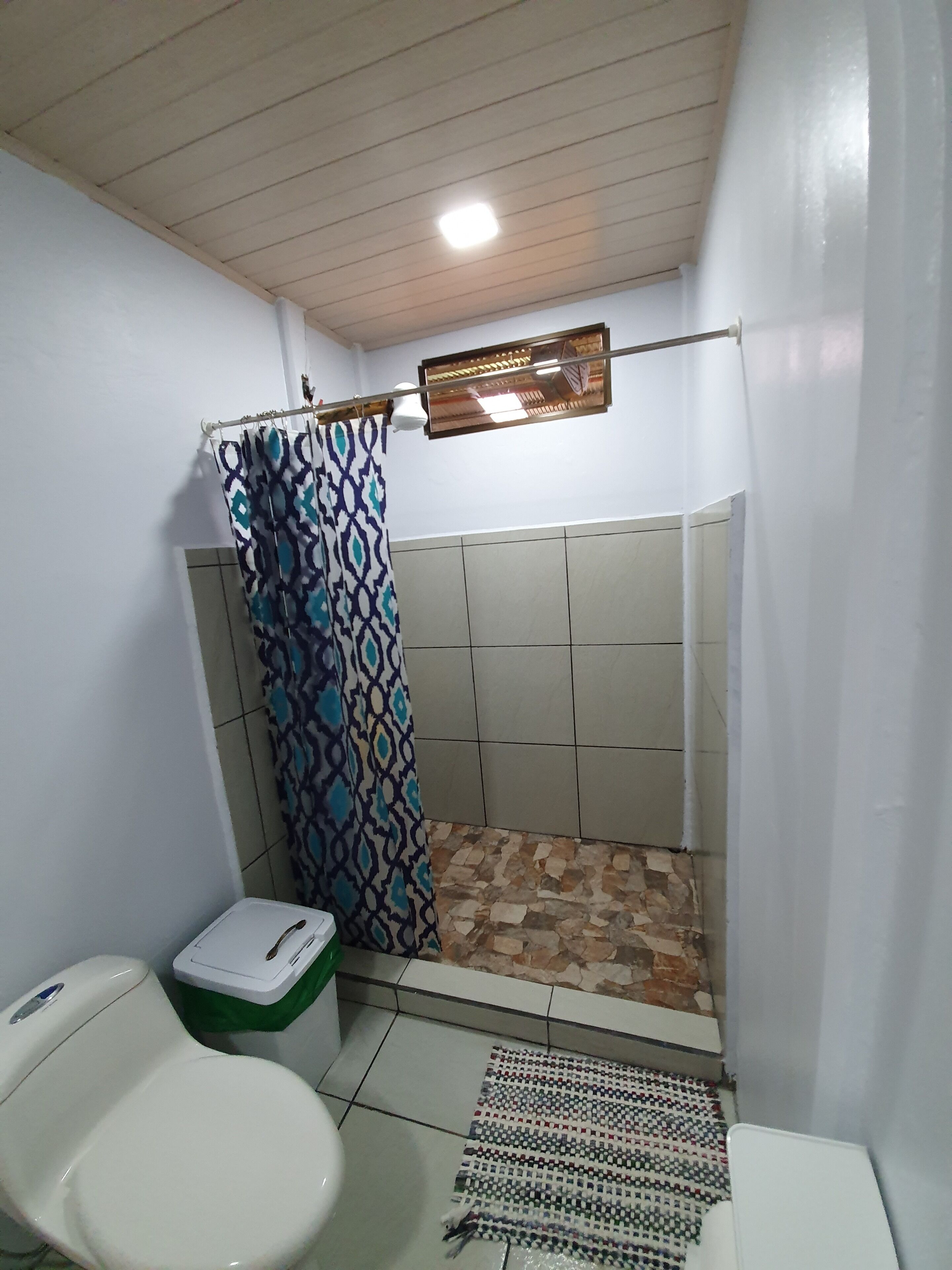 A small bathroom with a toilet, a shower with a patterned curtain, and a tiled floor.