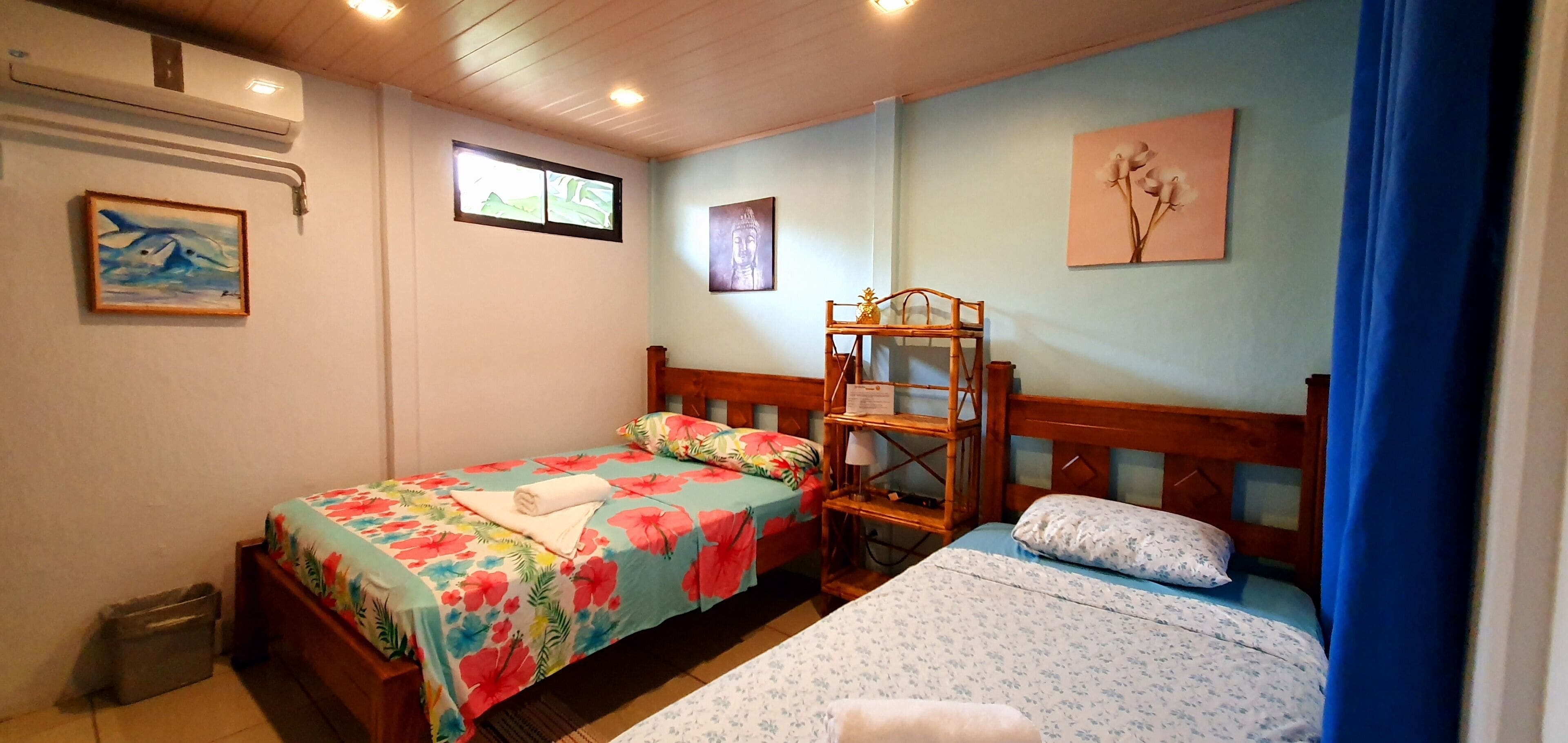 A room with two beds, a wooden headboard, a small shelf, and a window.