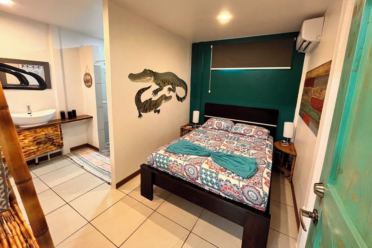 A bedroom with a bed, a bathroom with a sink, and a wall with a crocodile decal.