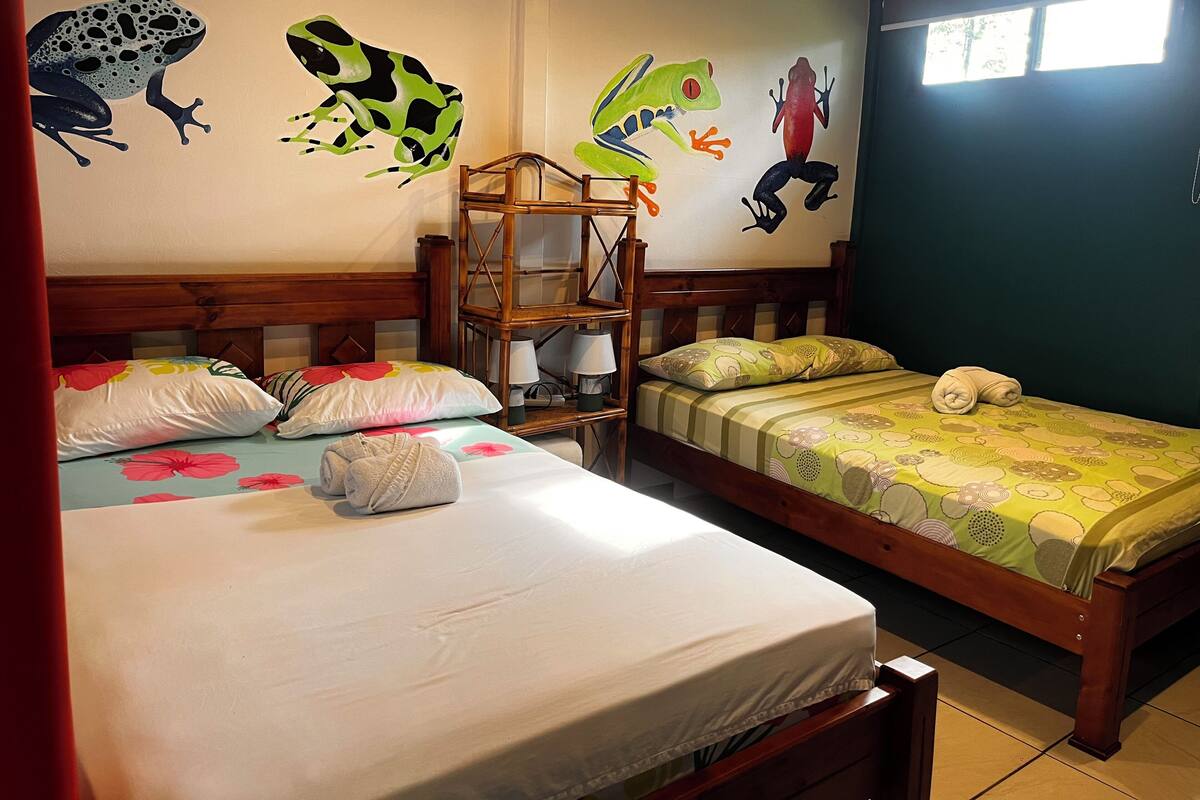 A bedroom with two beds, a wooden headboard, a nightstand, and a wall with colorful frog decals.