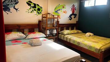 A bedroom with two beds, a wooden headboard, a nightstand, and a wall with colorful frog decals.