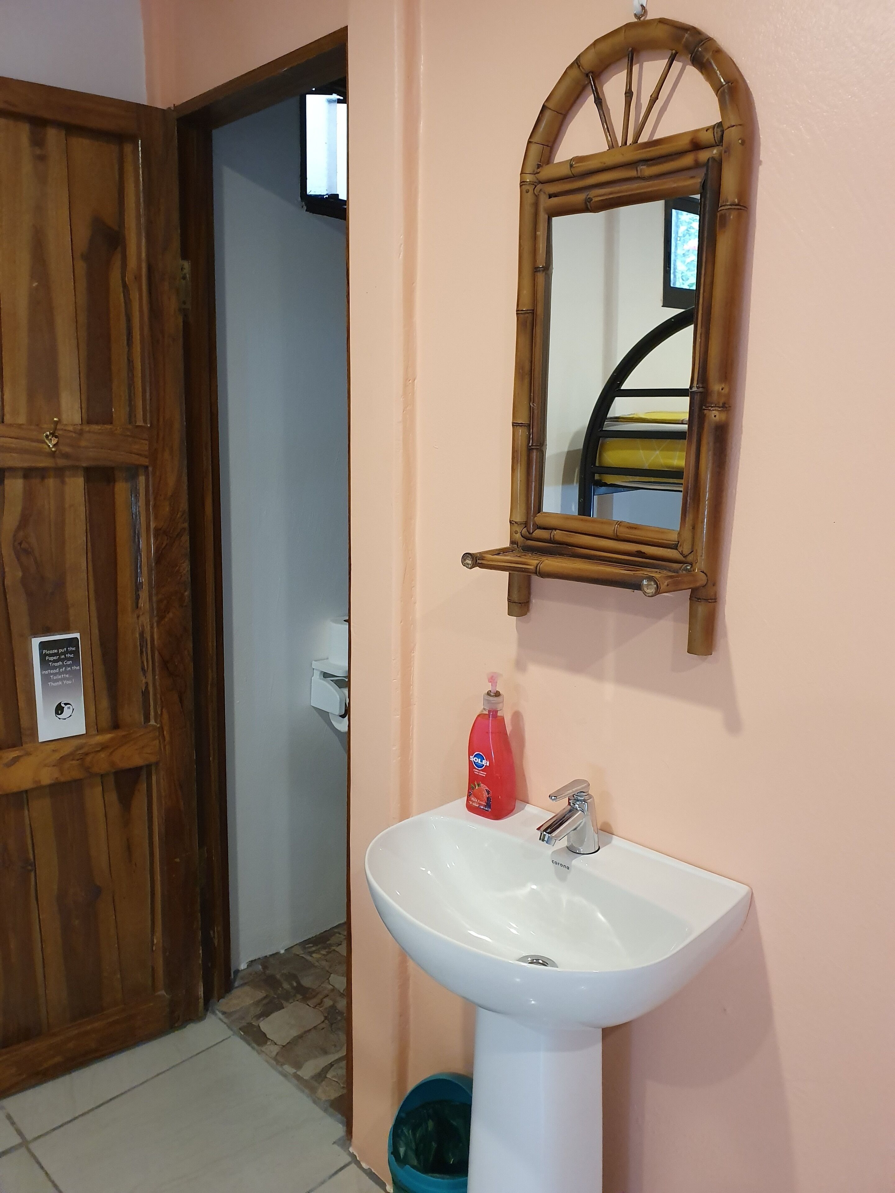 A bathroom with a wooden door, a white sink, a mirror, and a soap dispenser.