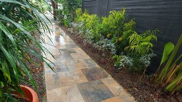 A pathway with stone tiles, surrounded by various plants and a black fence.