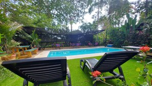 A pool area with two lounge chairs, a covered seating area, and surrounding greenery. - Hotel Tucan (Bahía Ballena)