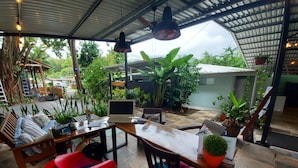 A covered outdoor area with a wooden table, chairs, and a laptop. There are potted plants and a view of greenery outside. - Hotel Tucan (Bahía Ballena)