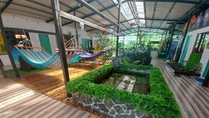A spacious indoor area with a wooden floor, a small water feature, and a hammock. - Hotel Tucan (Bahía Ballena)