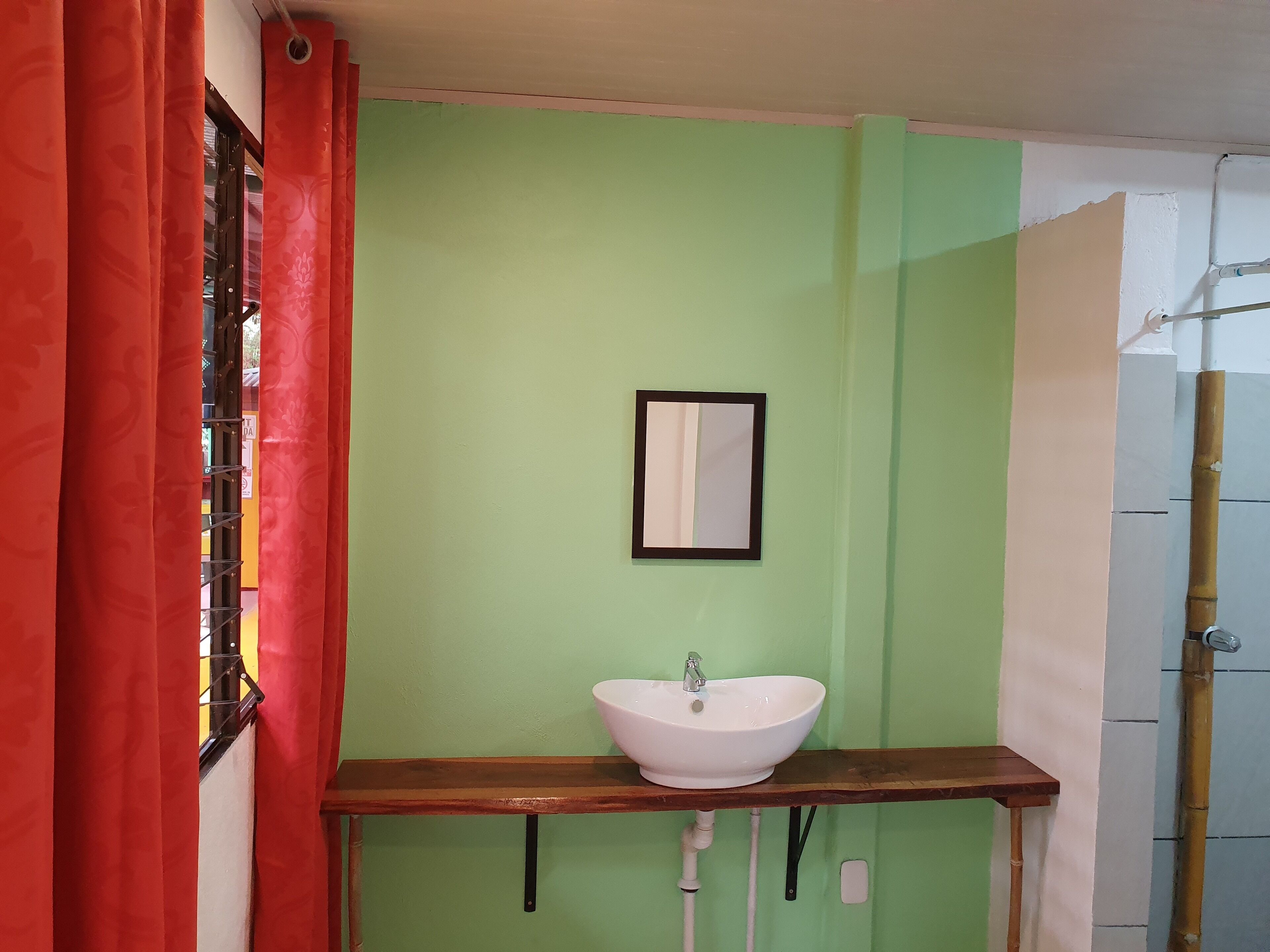 A bathroom with a green wall, a white sink, and a wooden shelf.
