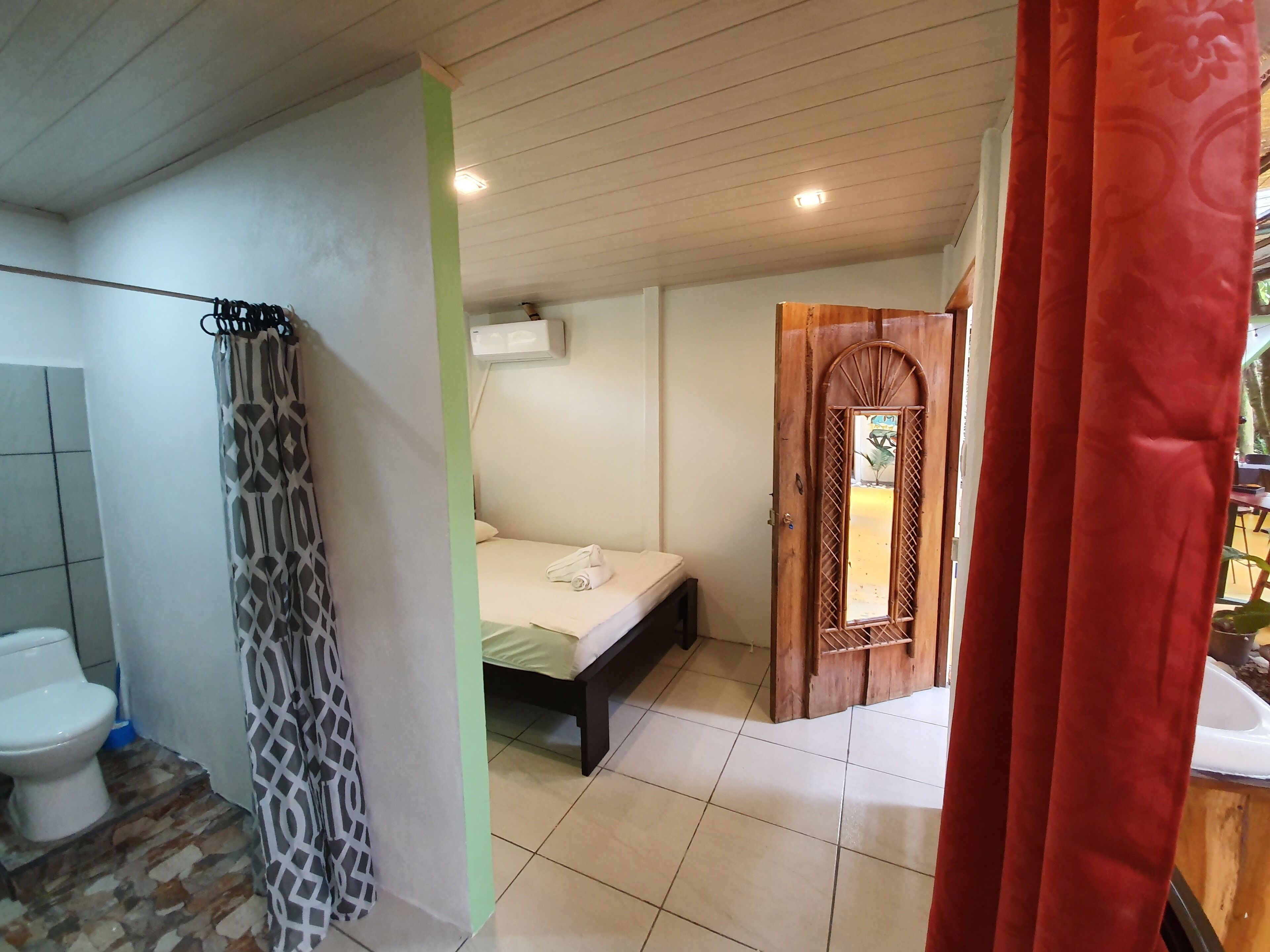 Une salle de bain avec des toilettes, un rideau de douche et un lit doté d’une porte en bois.